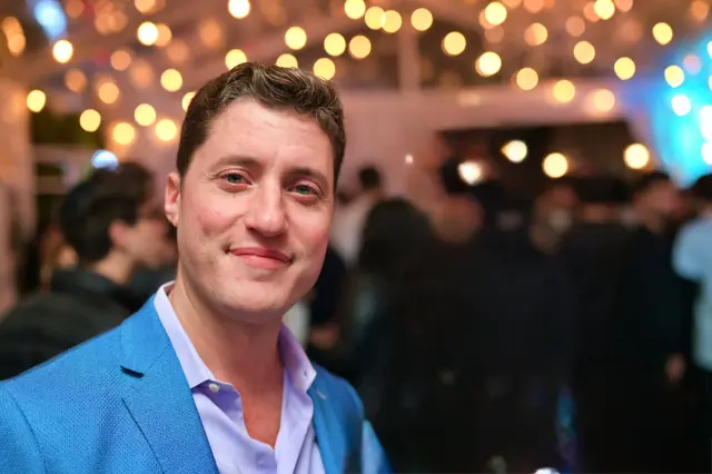 Man in a blue blazer at a lit-up party