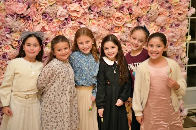 Six girls smiling in front of a flower wall